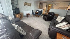 A living room with leather sofas, a television, a dining area with chairs, and a kitchen in the background. - Spring Garden Guest House (Gosport)