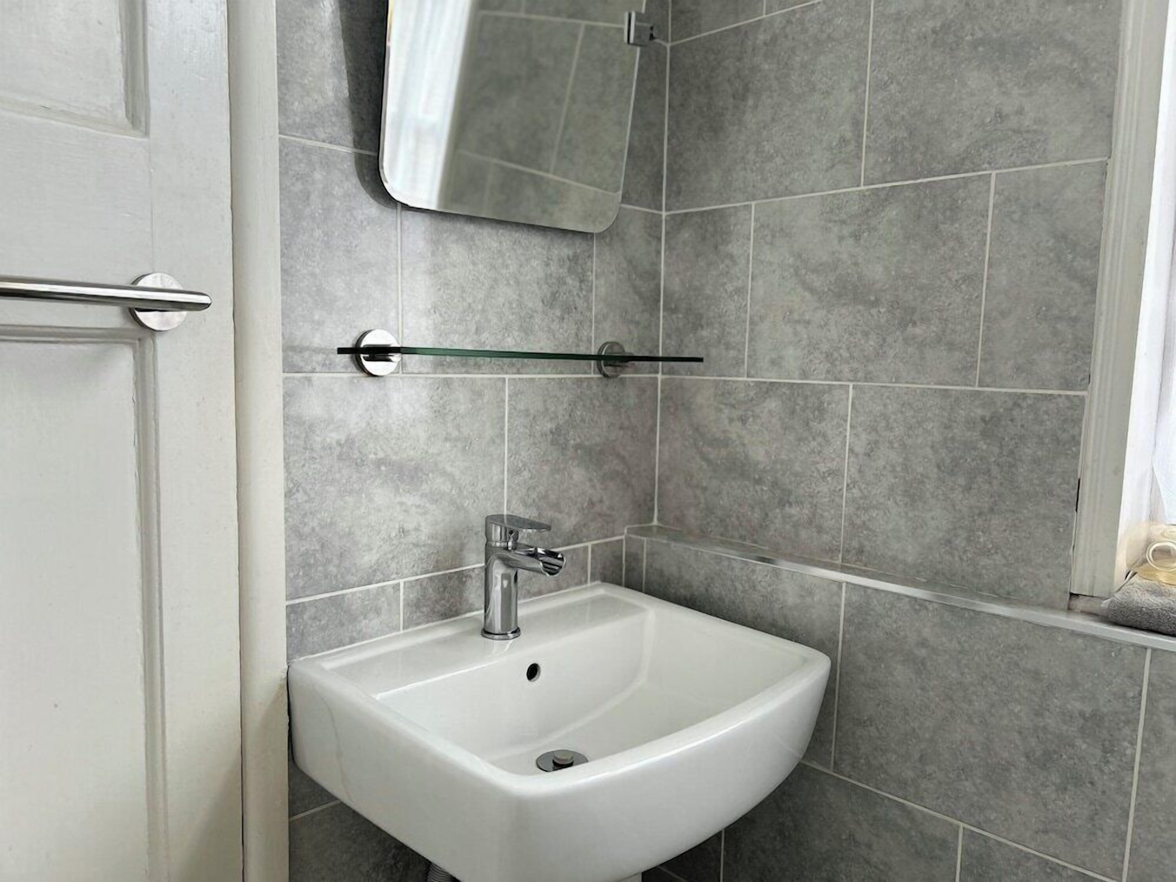 A bathroom with a white sink, a mirror above it, and grey tiled walls.