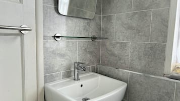 A bathroom with a white sink, a mirror above it, and grey tiled walls.