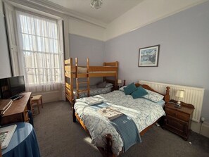 A bedroom with bunk beds, a desk with a computer, and a window with sheer curtains.
