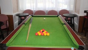 A pool table with balls and cues, surrounded by chairs and tables, in a room with large windows and curtains. - Spring Garden Guest House (Gosport)