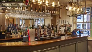 Un espace bar avec un assortiment de bouteilles et de verres, une caisse enregistreuse et une vue sur l’extérieur par une fenêtre.
