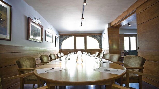 Une salle de conférence avec une longue table, des chaises, des tableaux encadrés aux murs et de grandes fenêtres.