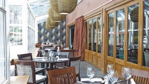 Un restaurant avec des tables et des chaises rondes, de grandes fenêtres et un mur décoré de motifs.