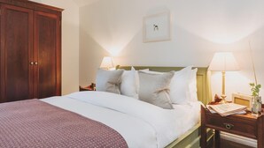 Un lit bien fait, avec du linge de lit blanc et un couvre-lit à motifs, une armoire en bois, une table de chevet avec une lampe et un tableau encadré au mur.