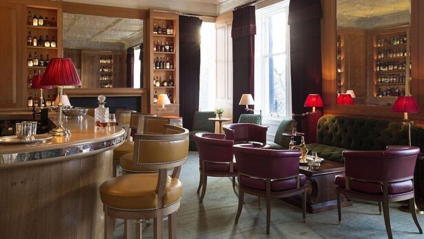 Un espace bar doté d’un comptoir circulaire, de plusieurs options d’assises, notamment des chaises et un canapé, ainsi que d’un grand miroir qui reflète la pièce.