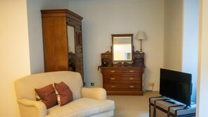 Un salon avec un canapé beige, un meuble en bois, un téléviseur posé sur un meuble et un miroir au-dessus du meuble.