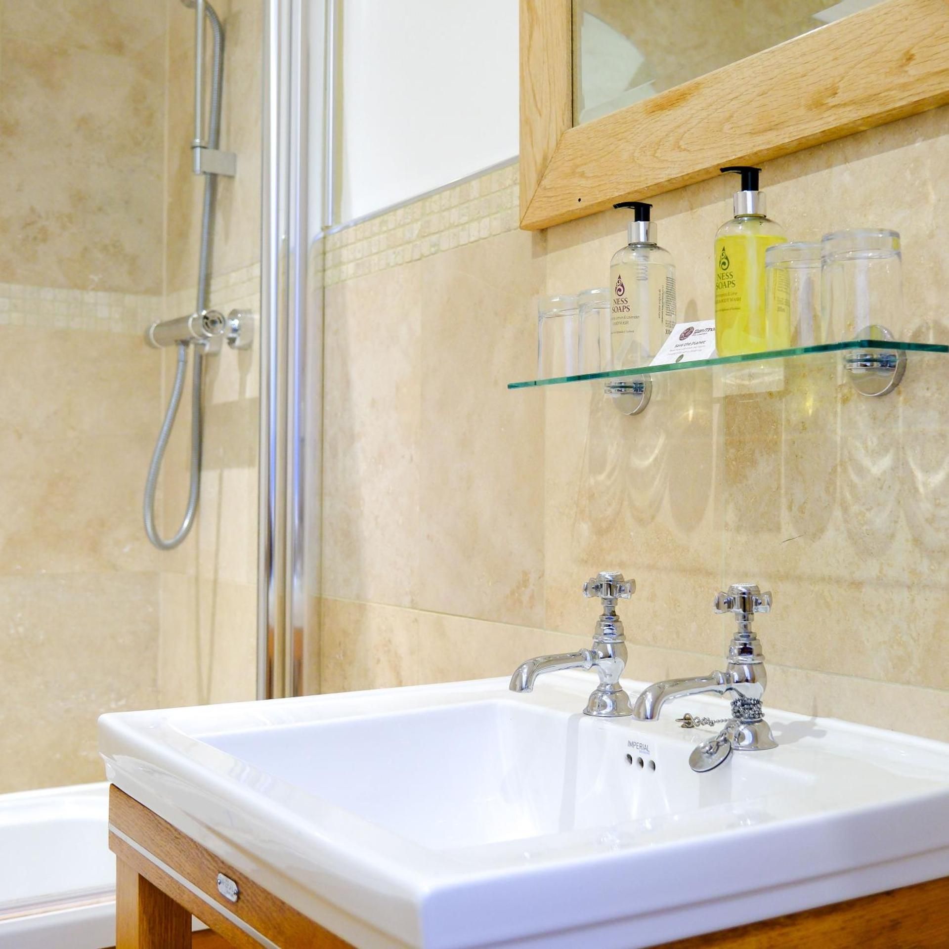 A bathroom with a white sink, two faucets, a glass shelf with toiletries, and a shower area.