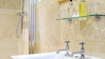 A bathroom with a white sink, two faucets, a glass shelf with toiletries, and a shower area.
