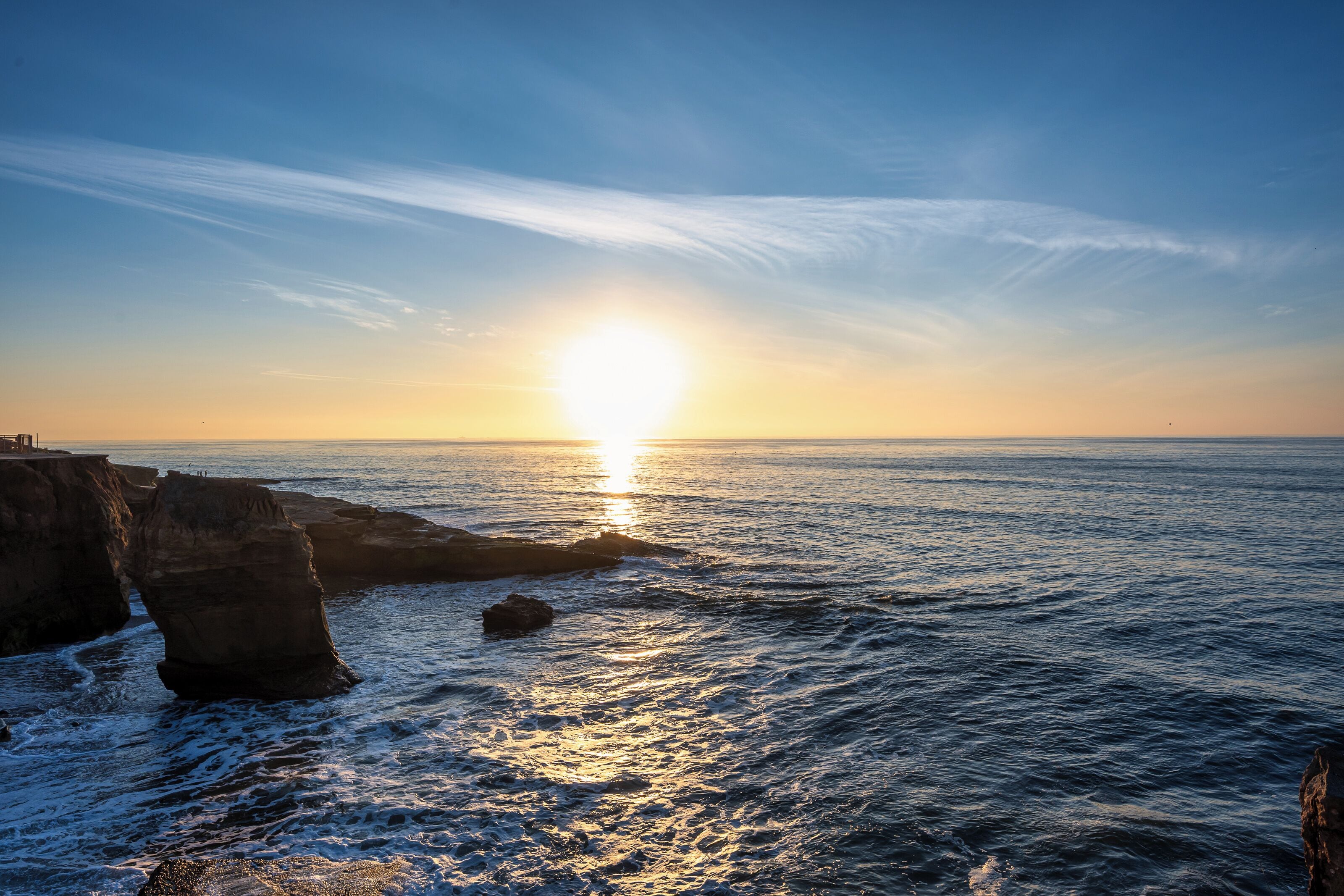 A coastal sunset with rocky cliffs and calm sea.