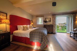 A bedroom with a large bed, a nightstand, a dresser, a window with curtains, and a view of the outdoors. - THE BAY Tree (Burford)