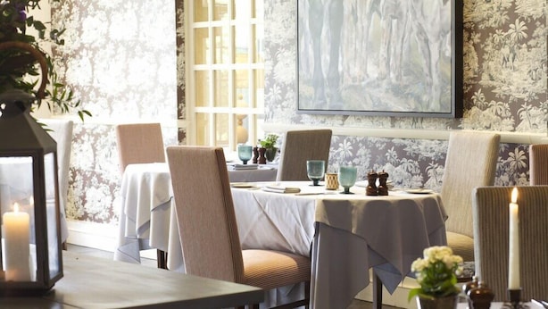A dining area with tables set for two, chairs, and a large painting on the wall. - The Bay Tree (Burford)