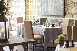 A dining area with tables set for two, chairs, and a large painting on the wall. - The Bay Tree (Burford)