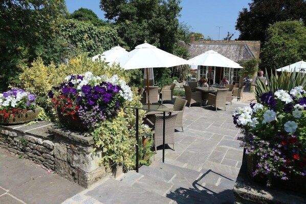 An outdoor patio area with stone flooring, wicker furniture, and white umbrellas. - The Bay Tree (Burford)