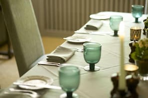 A neatly set dining table with green glassware and plates, a folded napkin, and candles. - THE BAY Tree (Burford)