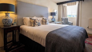 A hotel room with a large bed, two bedside tables with lamps, a chair, and a window with curtains. - The Bay Tree (Burford)