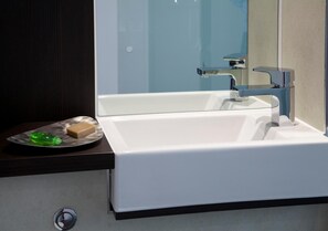 Une salle de bain moderne avec un lavabo blanc, un miroir et un plan de toilette foncé.
