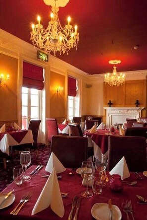 Un espace repas avec des tables dressées, un lustre et une cheminée.