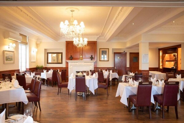 A formal dining room with multiple tables and chairs, a chandelier, and a fireplace. - Royal Hotel (Liverpool)