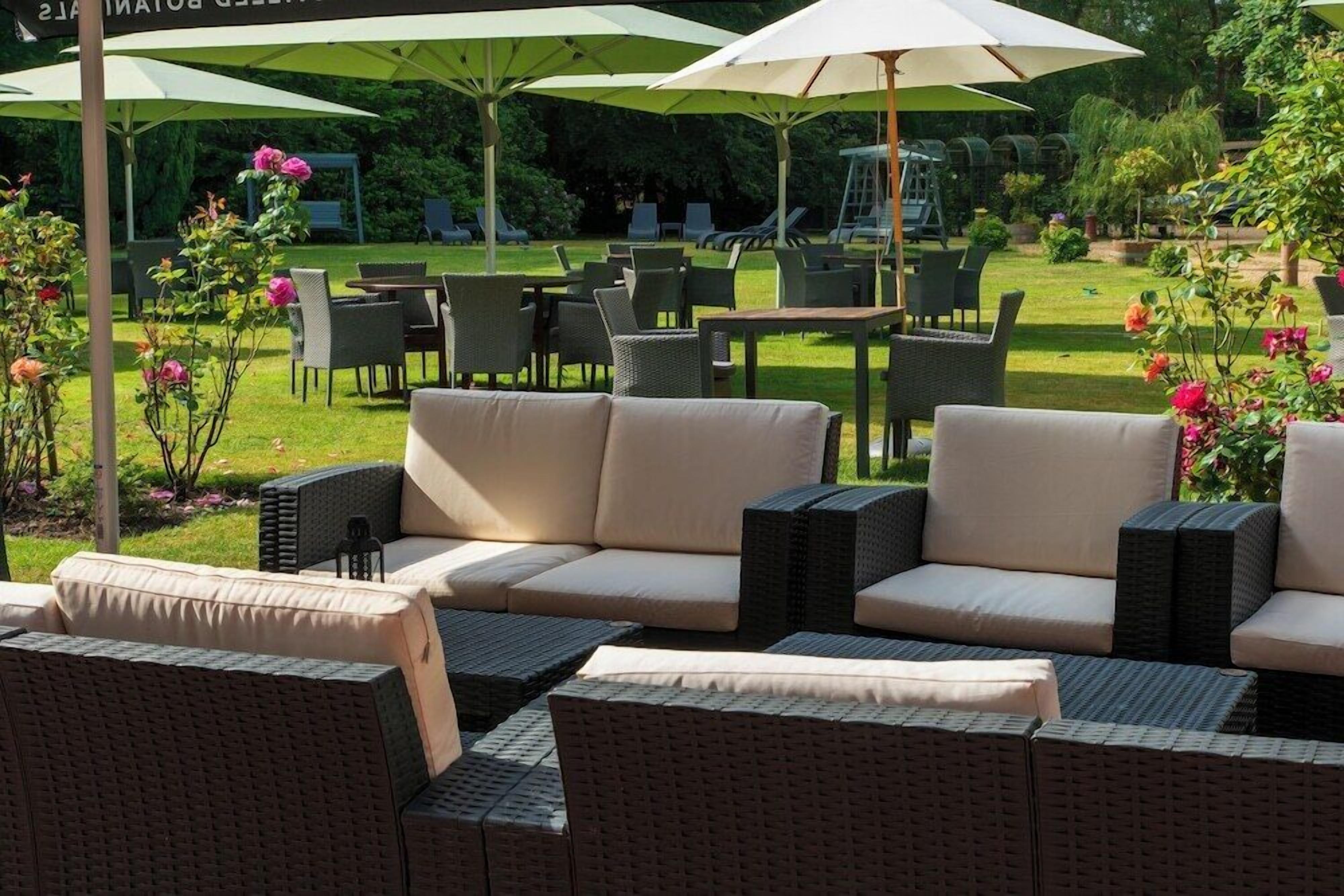 An outdoor seating area with wicker furniture and umbrellas, surrounded by greenery and flowers.