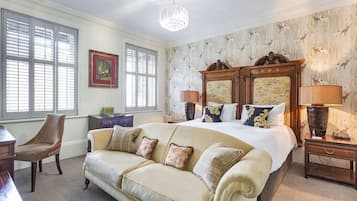 A bedroom with a large bed, a sofa, a desk, and a chair. There is a chandelier, a lamp, and a picture frame on the wall.