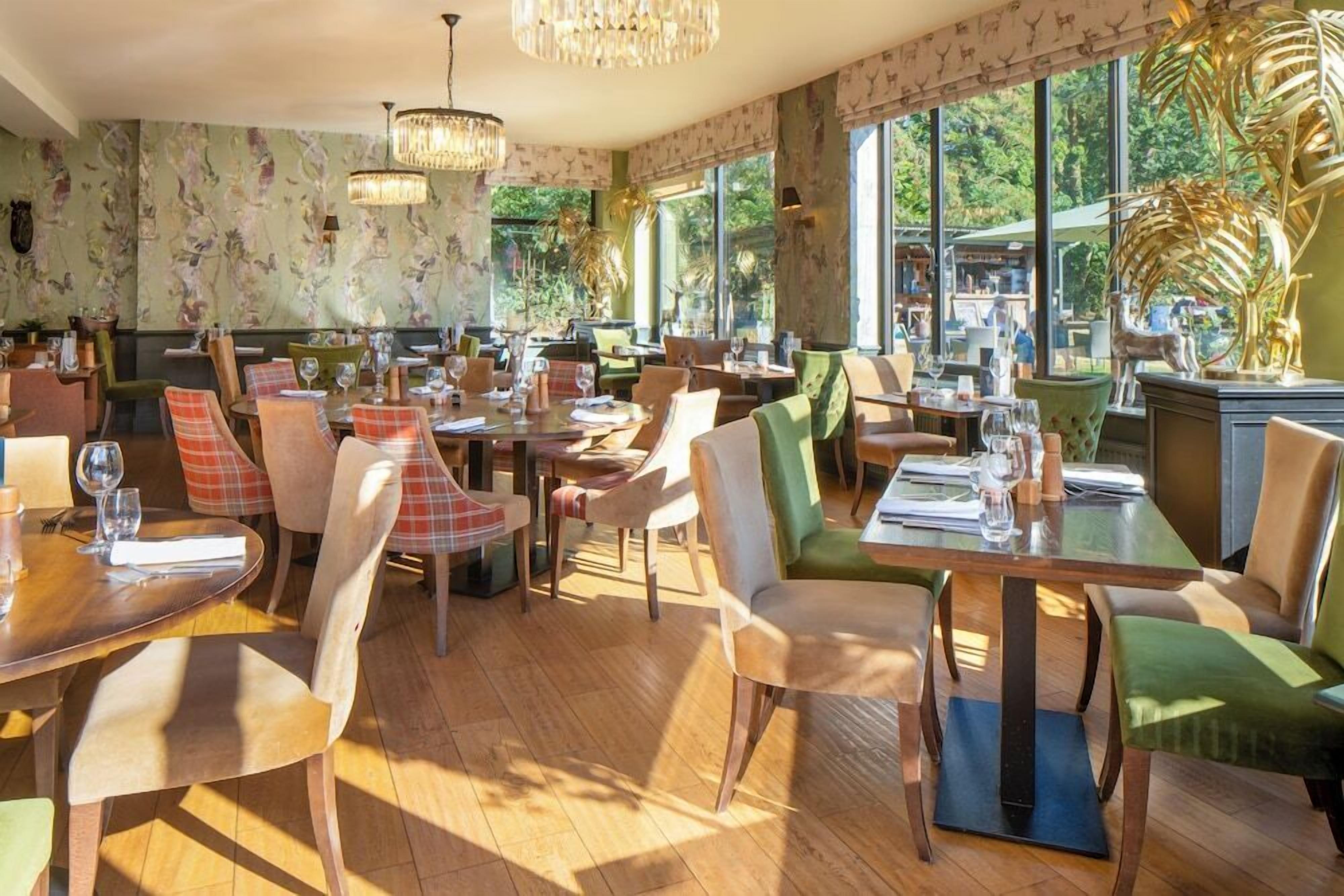 A restaurant with multiple dining tables and chairs, large windows with a view of greenery, and decorative elements like a golden palm sculpture.