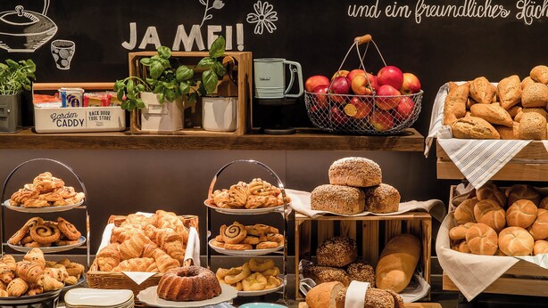 A bakery display with various baked goods, including bread, pastries, and a basket of apples. - Motel One (Newcastle-upon-Tyne)