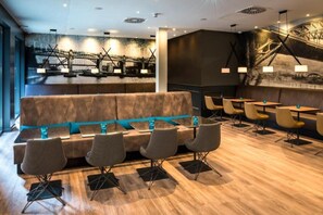 A modern restaurant with a wooden floor, a sofa with teal cushions, and multiple tables and chairs. - Motel ONE (Newcastle-upon-Tyne)