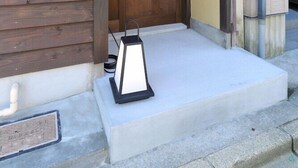 A wooden porch with a red cloth hanging, a lantern, and a concrete step leading to a door. - Kanazawa no Yado Ikedaya [vr] (Kanazawa)