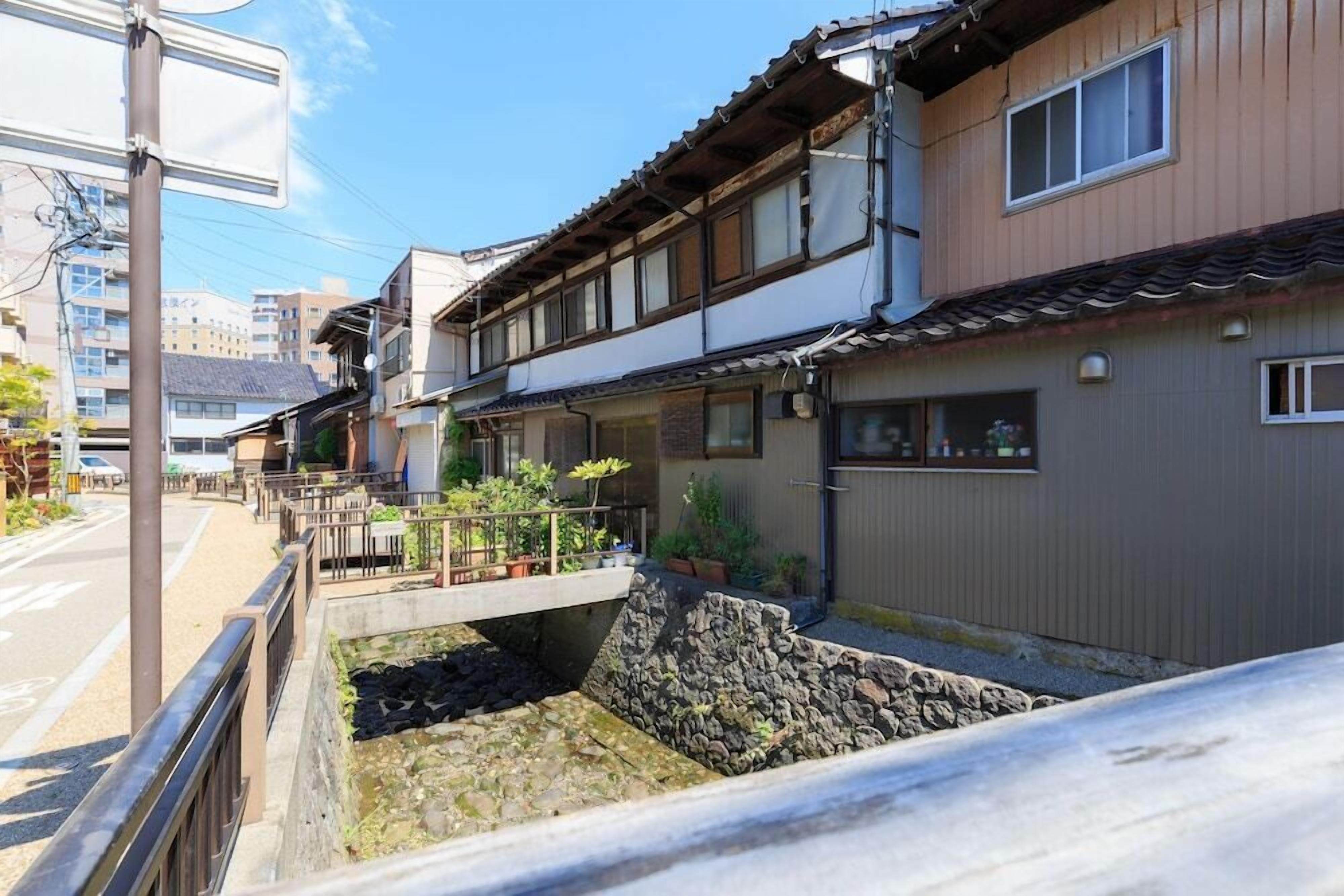 Ein traditionelles japanisches Wohngebäude mit einem Steinelement für Wasser, hölzernen Balkonen und einem Ziegeldach.