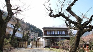 Een traditionele Japanse woning met een houten gevel, pannendak en een grindpad dat leidt naar een houten poort.