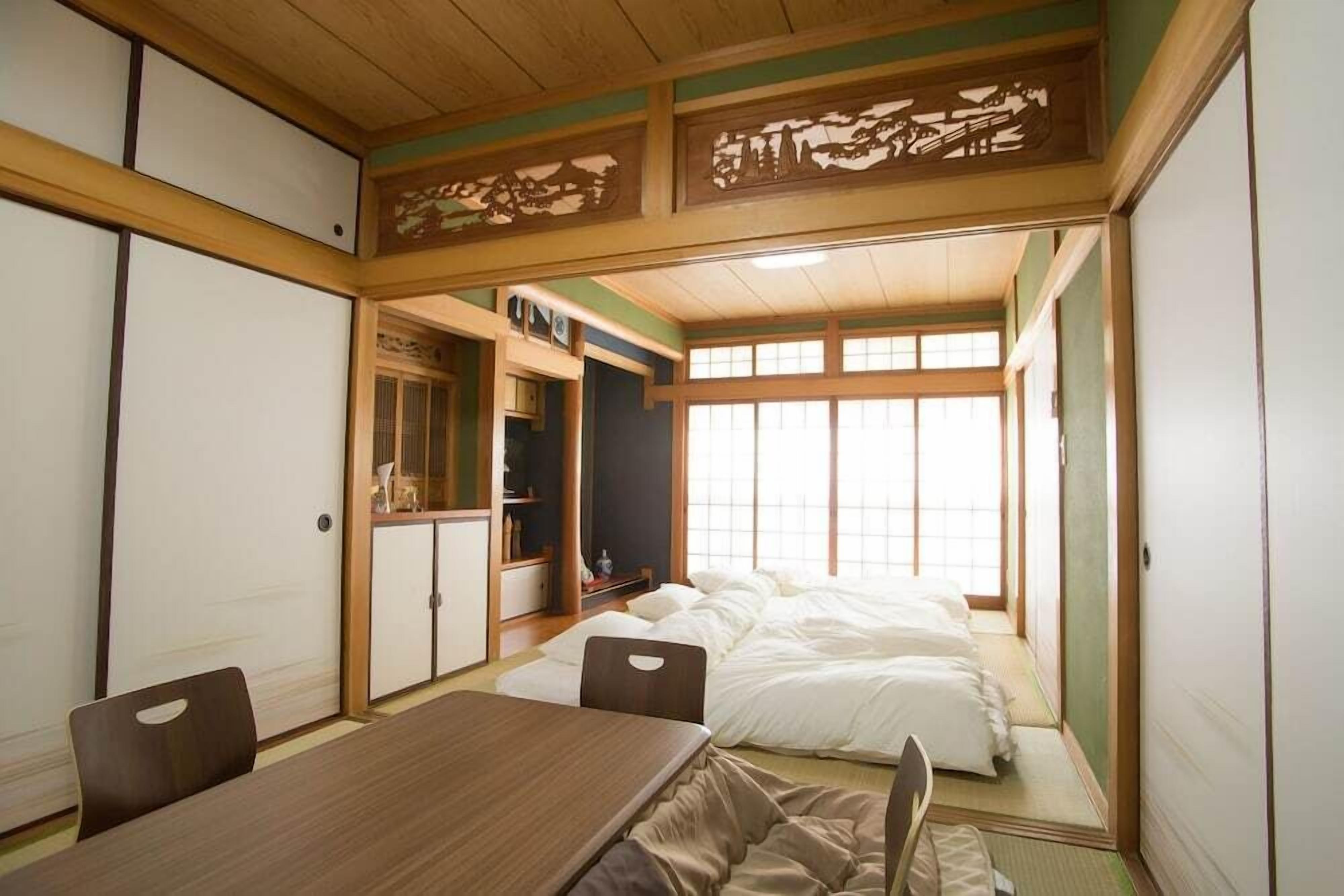 Una habitación tradicional japonesa con suelo de tatami, una mesa baja y una cama con ropa blanca.