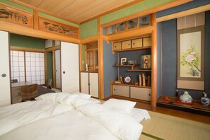 A traditional Japanese-style bedroom with tatami flooring, a low wooden bed, and a shoji screen door. - Dougo-yado Guest House [vr] (Matsuyama)