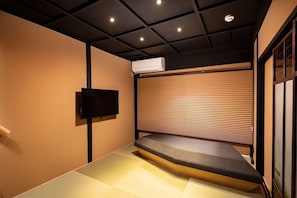 A room with tatami flooring, a low platform bed, a mounted TV, and a ceiling with recessed lighting. - Tsumugi Hachijo Minamotocho (Kyoto)