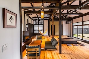 Ein modernes Interieur mit Holzboden, einer Hängematte, einem Sofa, einem Tisch und einem großen Fenster.