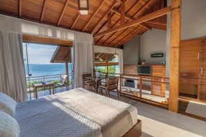Un dormitorio con una cama grande, un balcón con mesa y sillas, y un televisor sobre un mueble de madera.