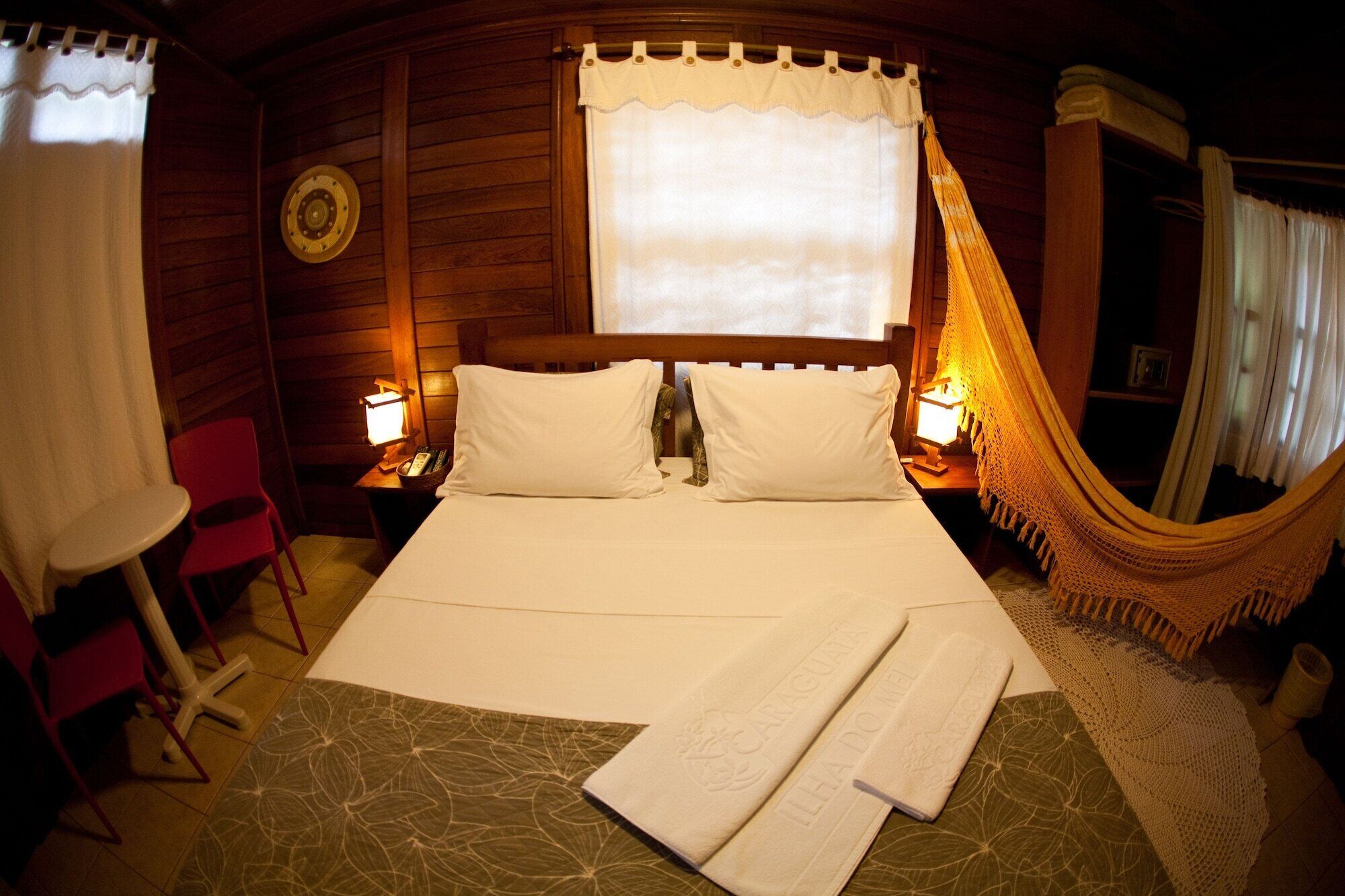 A cozy room with a bed, two bedside lamps, a hammock, and a small table with a chair.