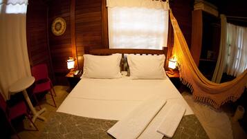 A cozy room with a bed, two bedside lamps, a hammock, and a small table with a chair.