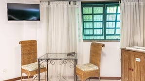 A room with a glass table, two wicker chairs, a wooden cabinet, a TV on the wall, and a window with green shutters. - Bomtempo Ii Chales Da Mata Ex Villaggio Imperiale Itaipava (Petrópolis)