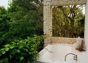 A stone wall with a metal railing, a white bathtub, and greenery in the background. - Hotel La Semilla (Playa del Carmen)