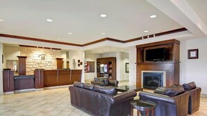 A spacious lobby with a stone fireplace, leather sofas, a flat-screen TV, and a reception desk. - Weyburn Canalta Hotel (Weyburn)