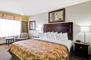 A hotel room with a large bed, a chair, a nightstand, a lamp, and a window with curtains. - Weyburn Canalta Hotel (Weyburn)