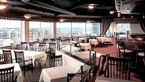 A restaurant with tables and chairs, large windows with a city view, and a high ceiling with exposed beams. - Casablanca Winery Inn (Grimsby)