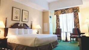 A hotel room with a large bed, two wall-mounted lamps, a small table with chairs, and a window with curtains. - Casablanca Winery Inn (Grimsby)