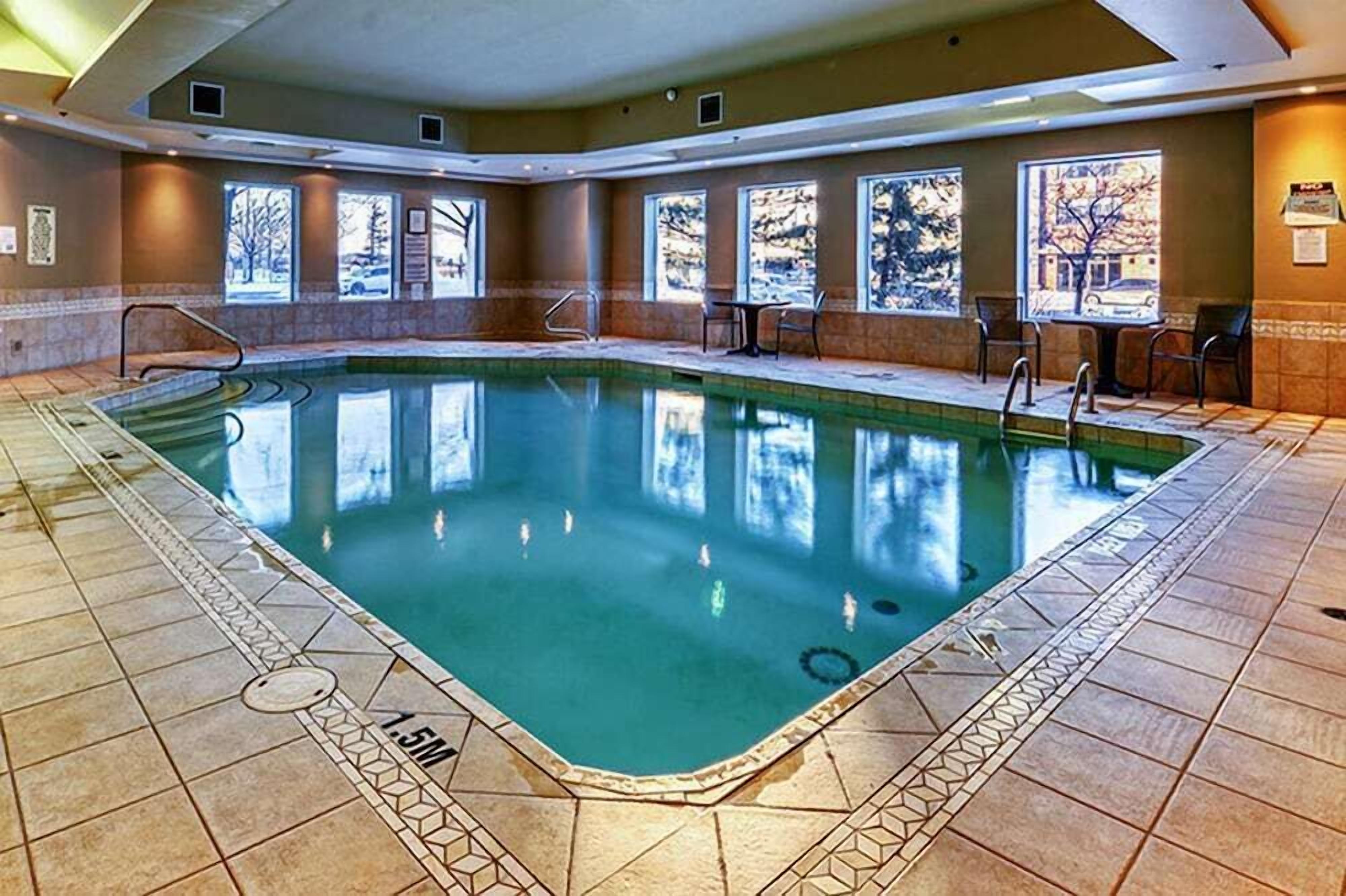 An indoor swimming pool with clear water, tiled floor, and windows with artwork.