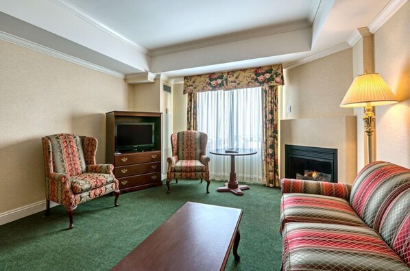 A hotel room with a green carpet, a sofa, a chair, a TV, a fireplace, and a table. - Casablanca Winery Inn (Grimsby)