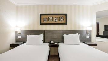 A hotel room with two beds, a headboard, a framed artwork above the beds, and a nightstand with a phone and lamp.