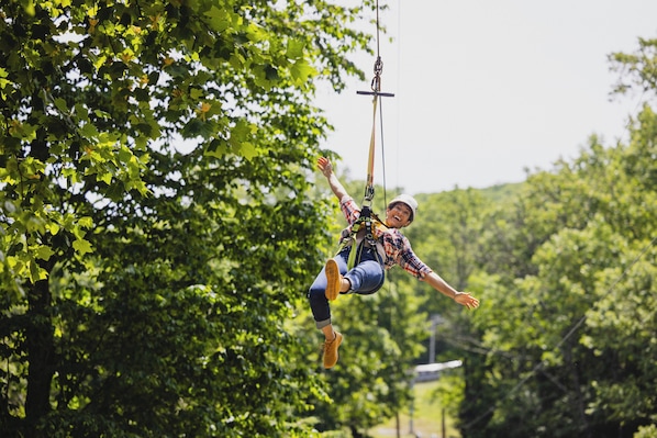 A person bungee jumping with a harness and helmet, surrounded by dense green foliage. - Camelback Lodge & Aquatopia Indoor Waterpark (Tannersville)