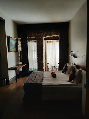 A hotel room with a bed, a desk, and a chair. There is a painting on the wall and a window with curtains. - Gumusyan Hotel (Istanbul)