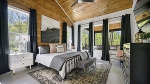 Un dormitorio con cama, mesitas de noche, un banco y vistas al exterior.
